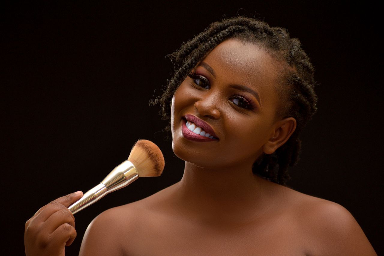 A beautiful smiling woman with braided hair holding a makeup brush against a black background.