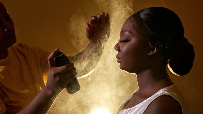 A stylist applying hairspray on a model's hair as part of beauty preparation indoors.