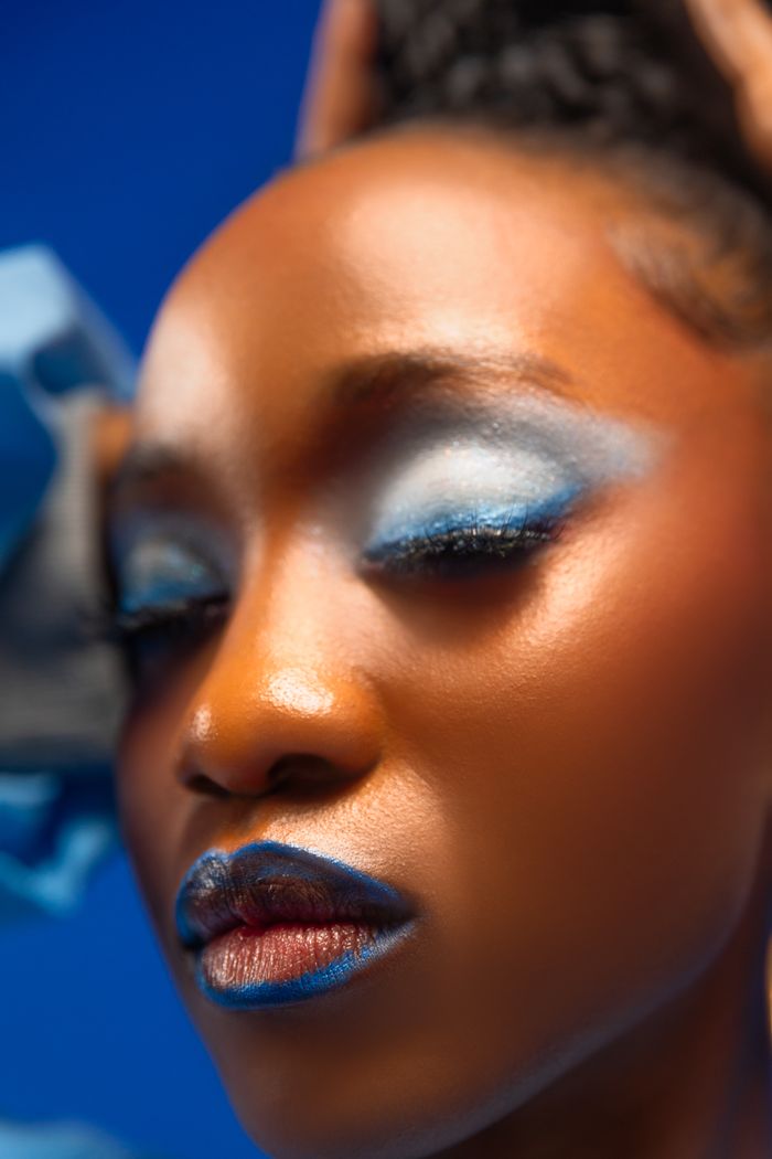 Stunning close-up of woman's face with vibrant blue eye makeup on a blue background.